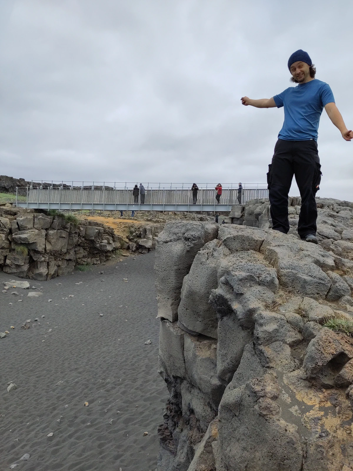 Ein Mann balanciert mit ausgebreiteten Armen auf einem Lavafelsen, im Hintergrund die Brücke über die Schlucht