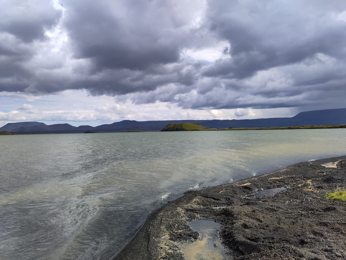 Dunkler Lavastrand am See unter schweren Wolken