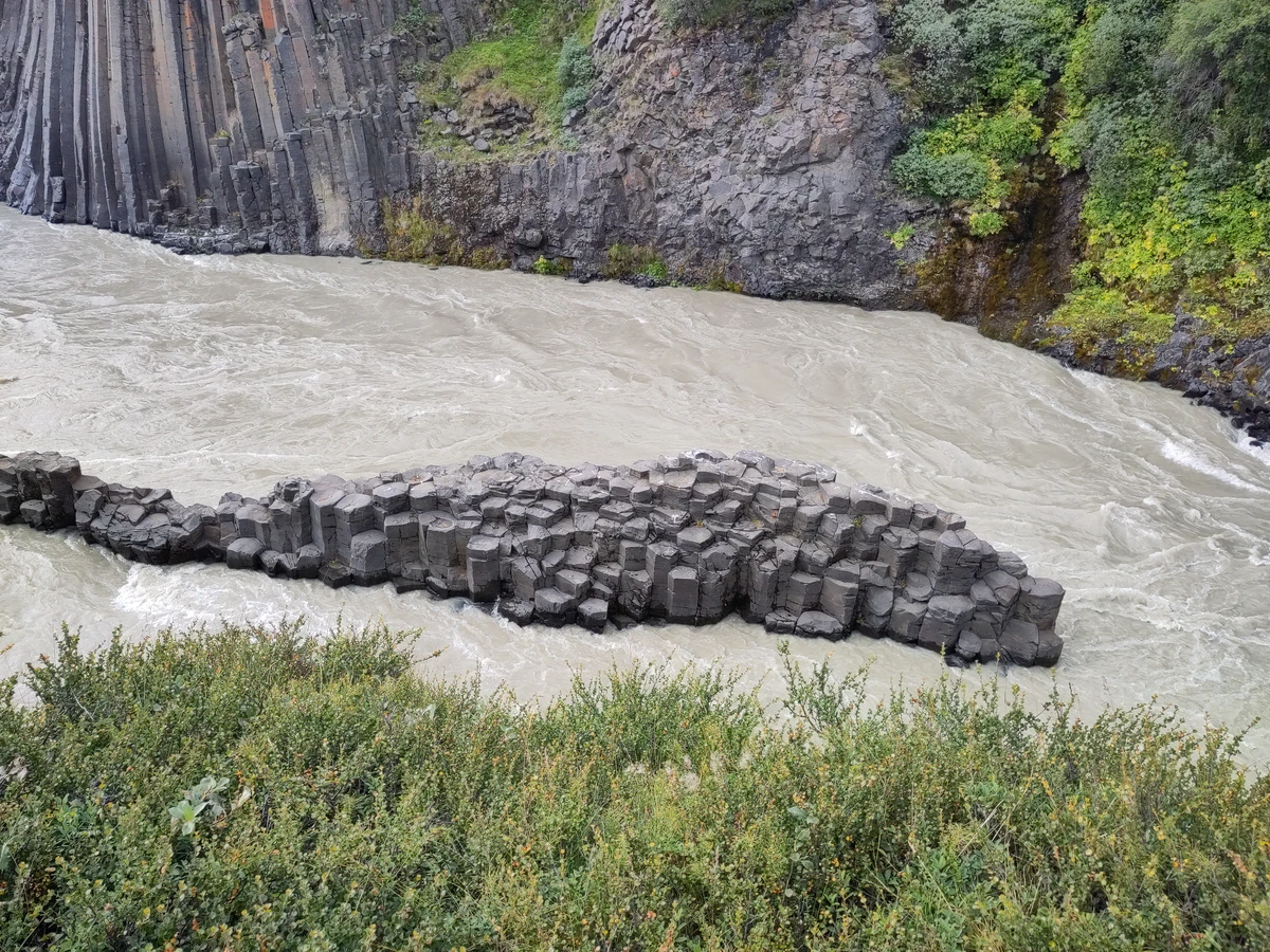 Insel aus sechseckigen Basaltsäulen im milchig-grauen Fluss