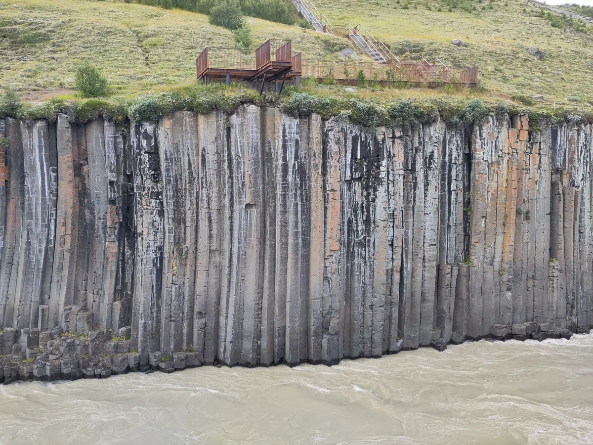 Wand aus senkrechten Basaltsäulen über dem Fluss, oben eine Aussichtsplattform