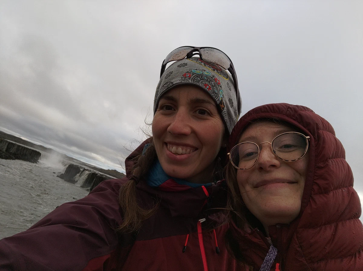 Selfie von zwei Frauen in dicken Jacken vor dem Wasserfall