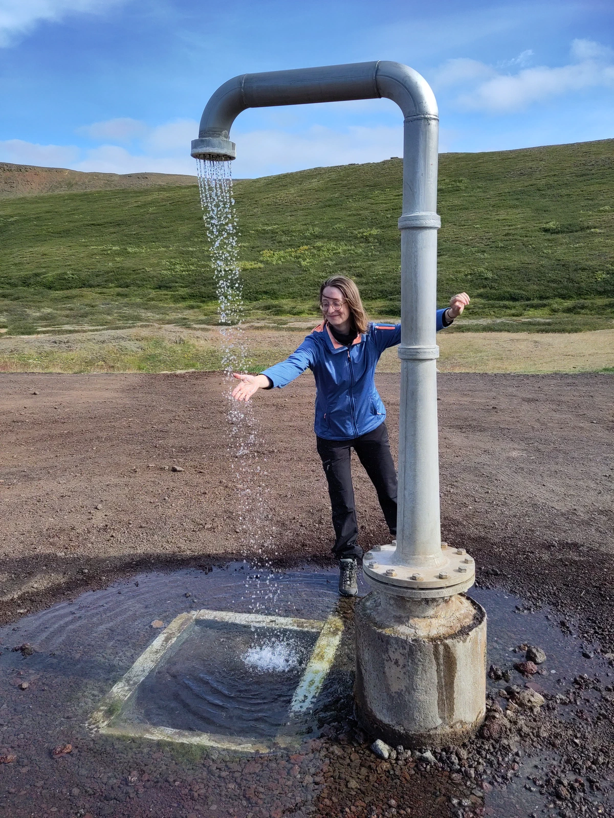 Eine Person steht mit ausgebreiteten Armen unter der endlosen Dusche, einem Rohr, aus dem ständig warmes Wasser läuft
