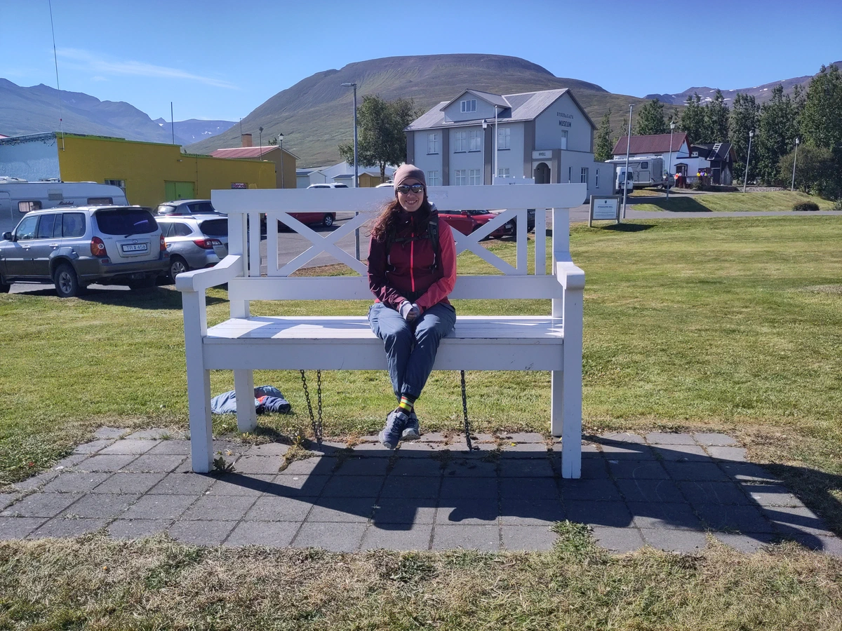 Eine Person sitzt auf einer übergroßen weißen Bank vor einem Haus in Dalvík