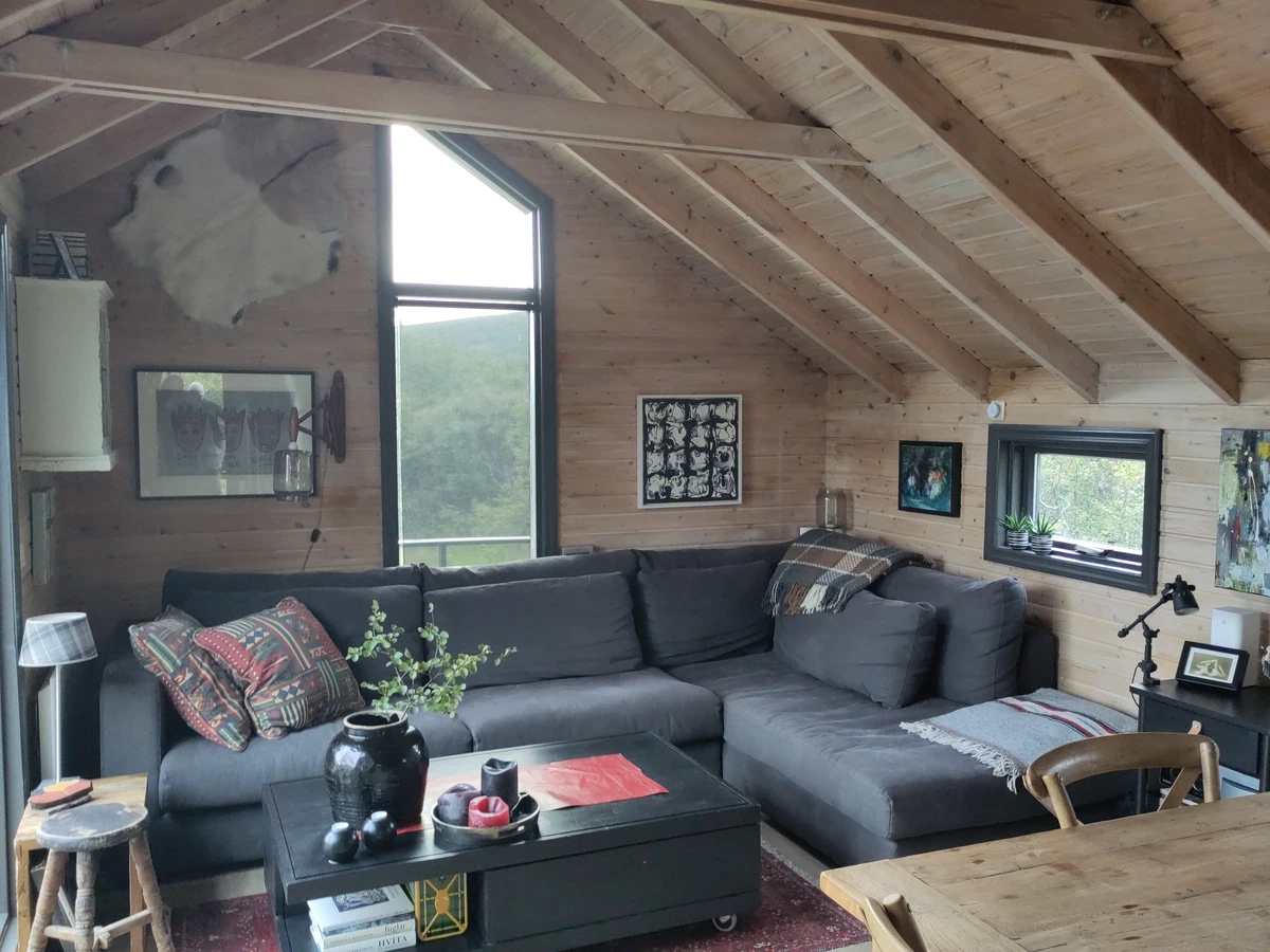 Wohnzimmer des Ferienhauses mit grauem Ecksofa unter einer offenen Holzdecke