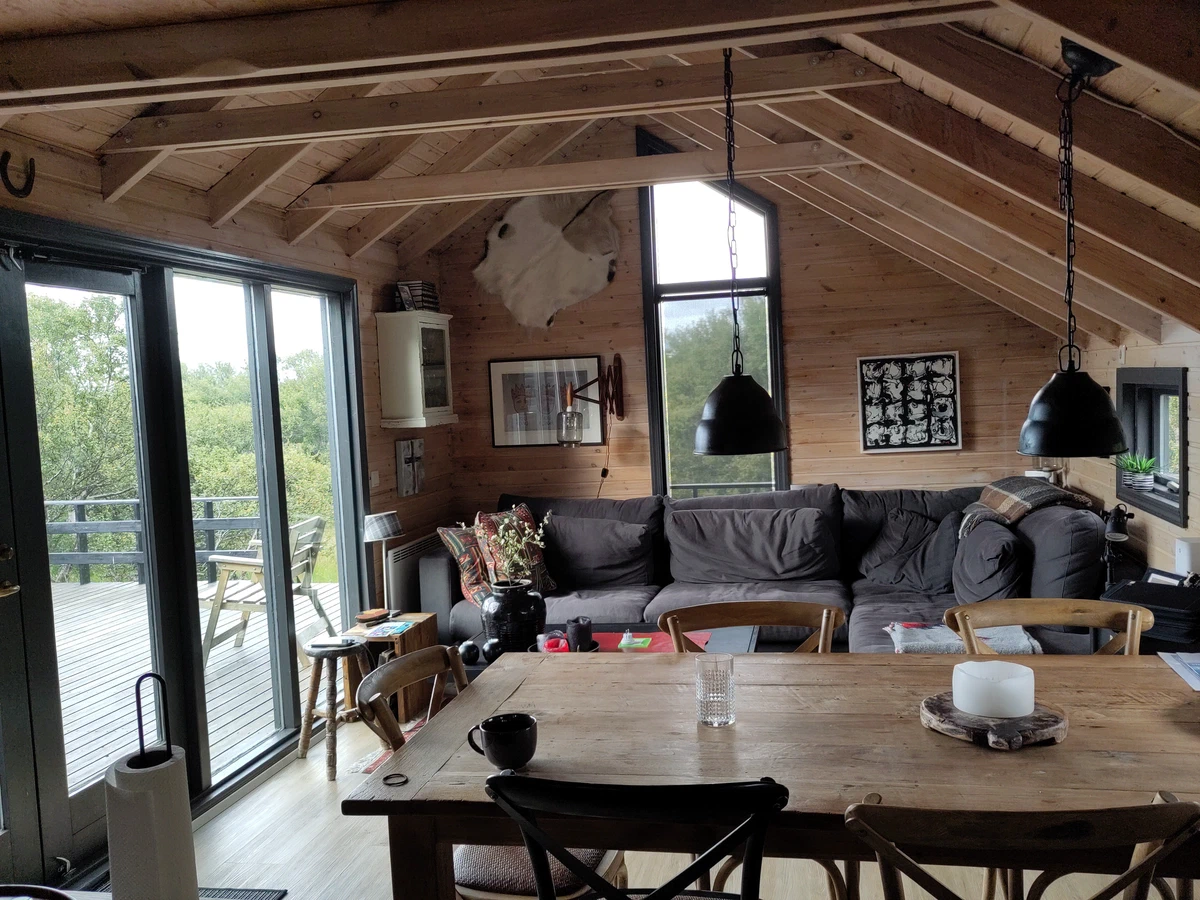 Wohn- und Essbereich des Holzhauses mit großem Tisch, Sofa und Blick auf die Terrasse
