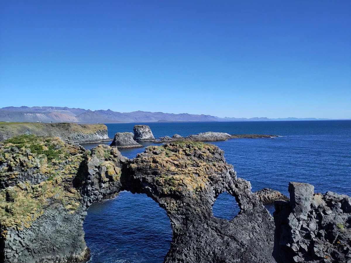 Felsbogen aus dunklem Basalt im tiefblauen Meer bei Arnarstapi