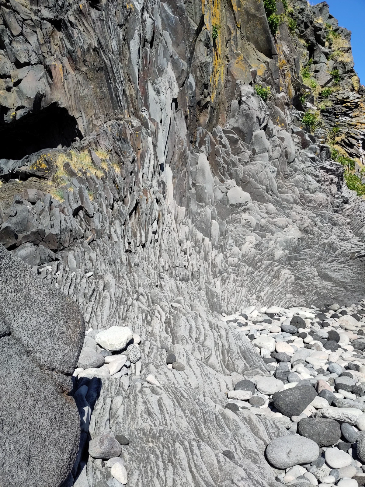 Steilwand aus fächerförmig angeordneten Basaltsäulen über einem Kieselstrand