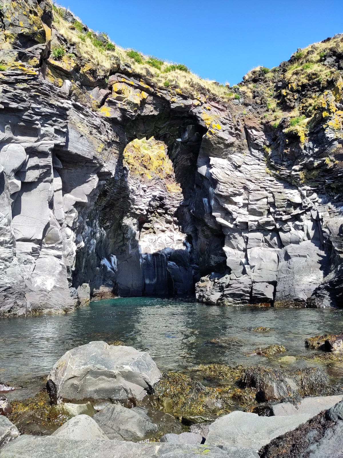 Felsentor aus Basalt über einem Gezeitentümpel