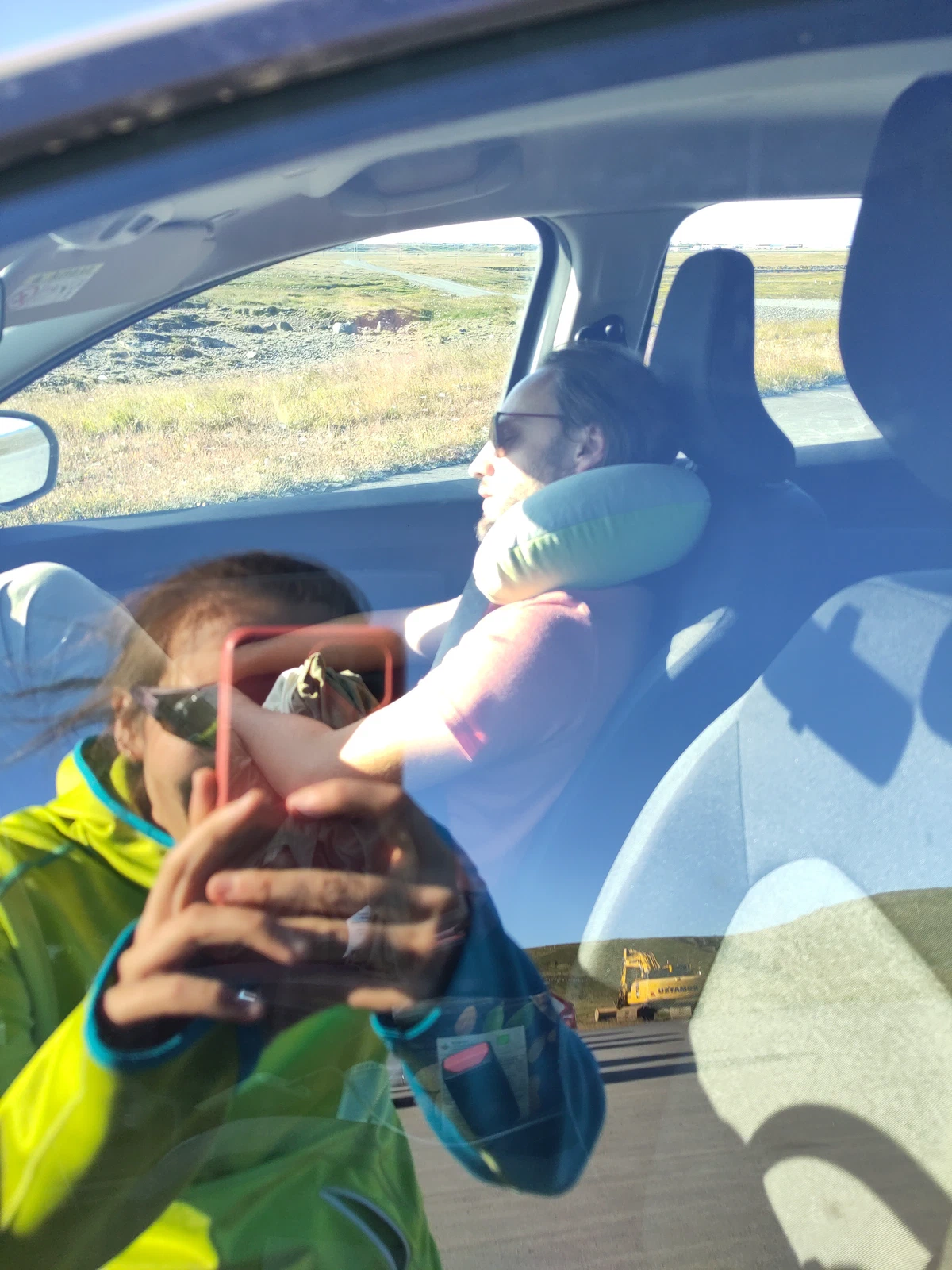 Spiegelung in der Autoscheibe: eine Person fotografiert die schlafende Mitfahrerin mit Nackenkissen