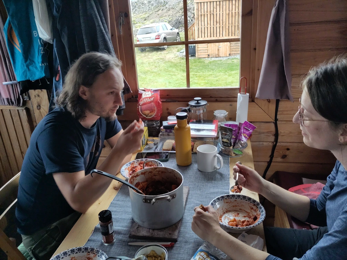 Zwei Personen essen am Tisch in der Holzhütte, in der Mitte ein Topf mit Tomatensauce