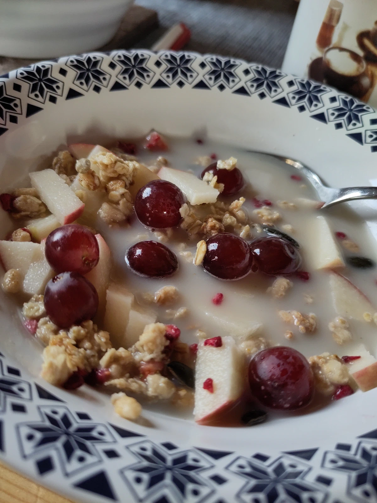 Müsli mit Apfelstücken, Trauben und Milch in einem blau gemusterten Teller