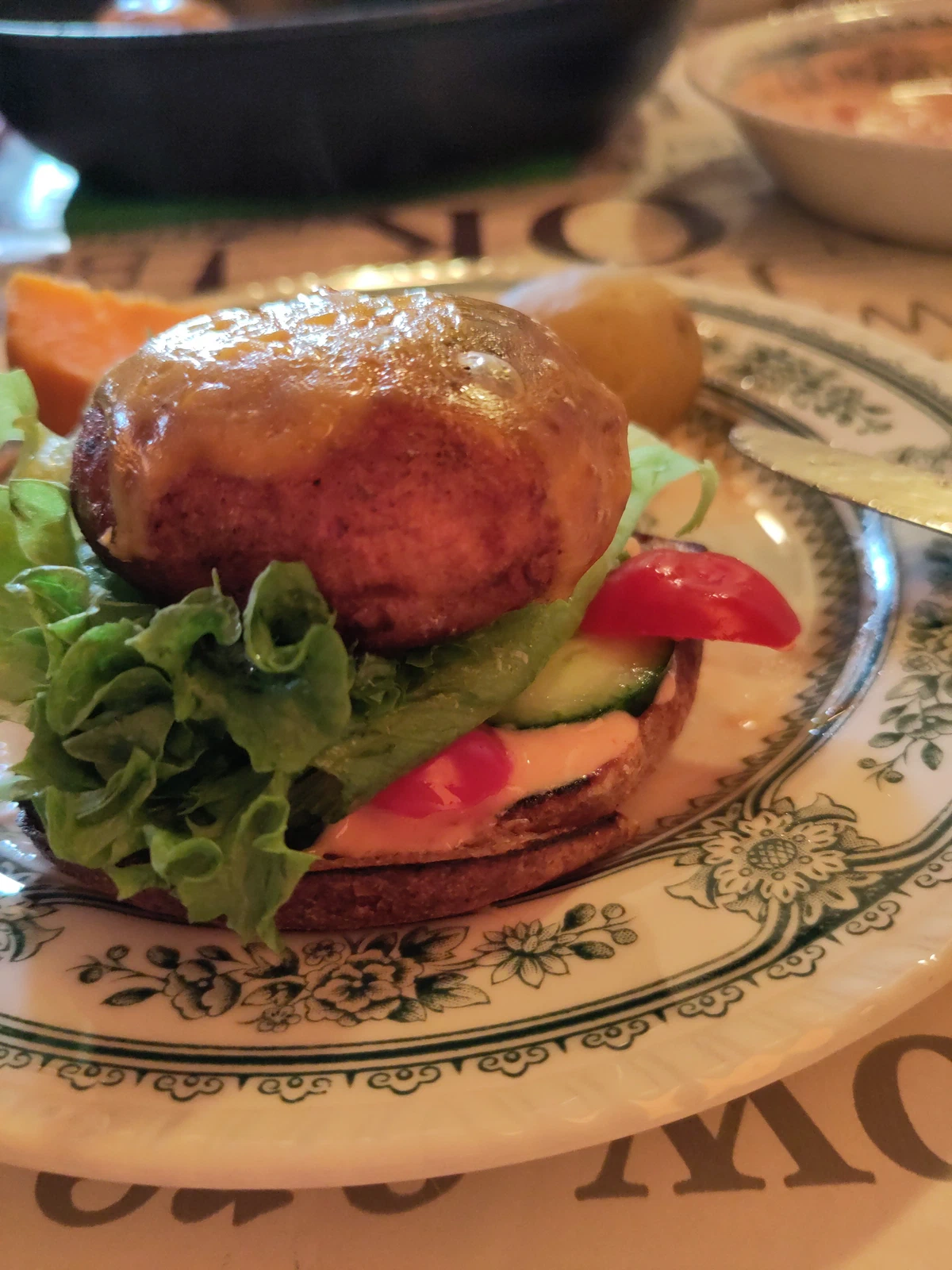 Burger mit Salat, Tomate und Gurke auf einem gemusterten Teller