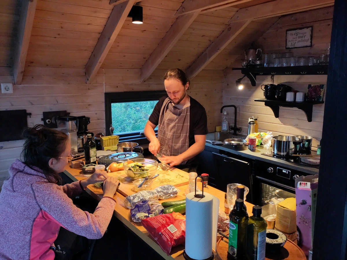 Zwei Personen schneiden gemeinsam Gemüse an der Kücheninsel des Holzhauses