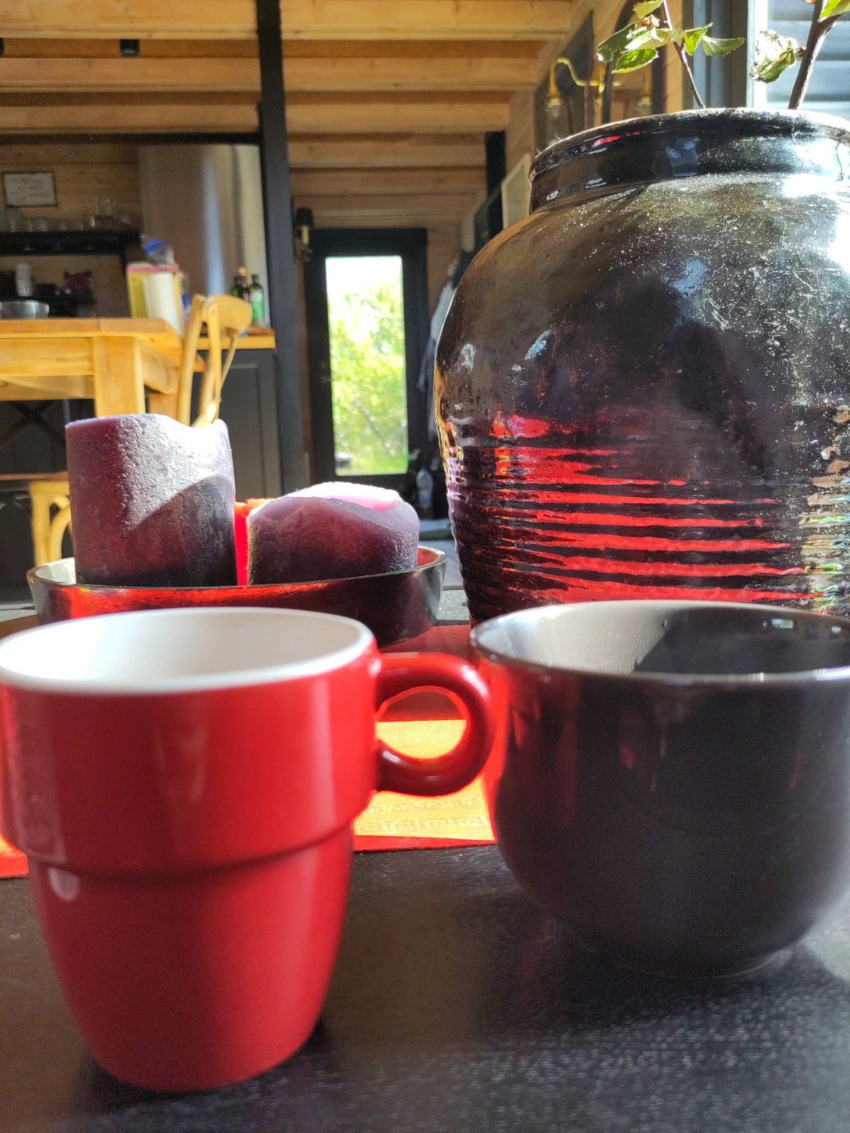 Zwei Kaffeetassen neben einer dunklen Vase auf dem Tisch