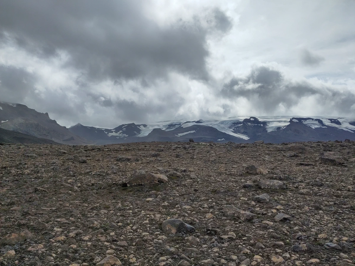 Steinwüste im Hochland, am Horizont Gletscherzungen unter dunklen Wolken