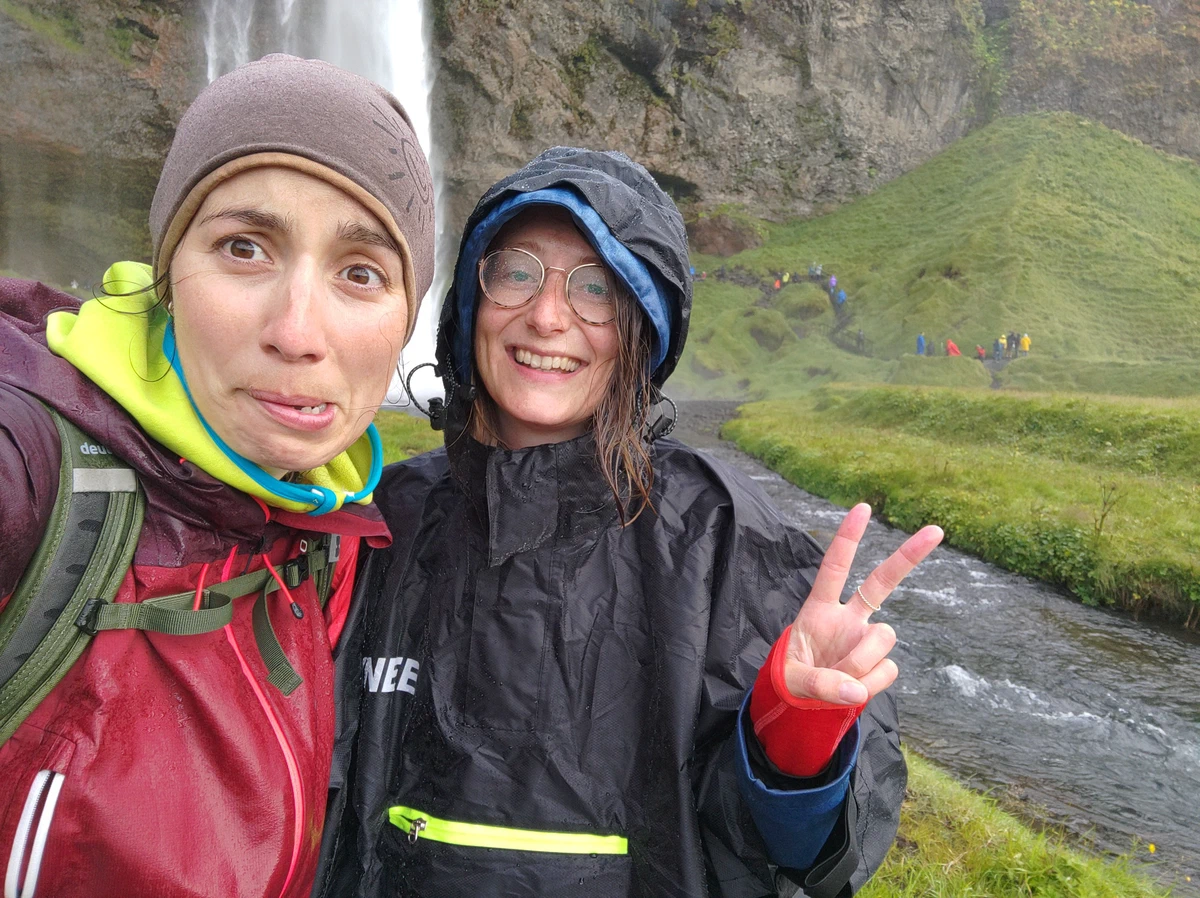 Selfie von zwei durchnässten Frauen in Regenjacken, eine macht das Peace-Zeichen