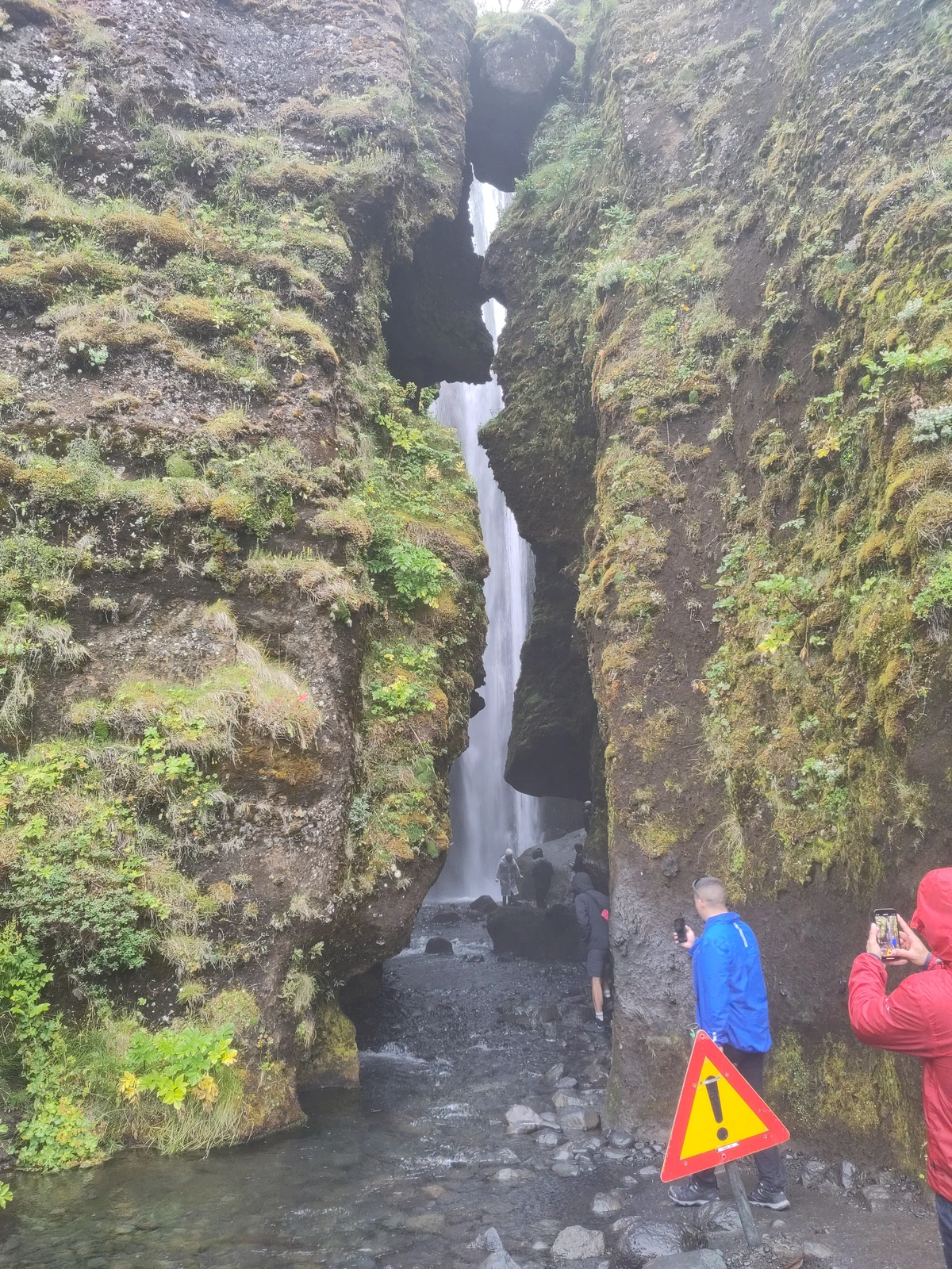 Eingang zur Felsspalte des Gljúfurárfoss mit Besuchern und einem Warnschild