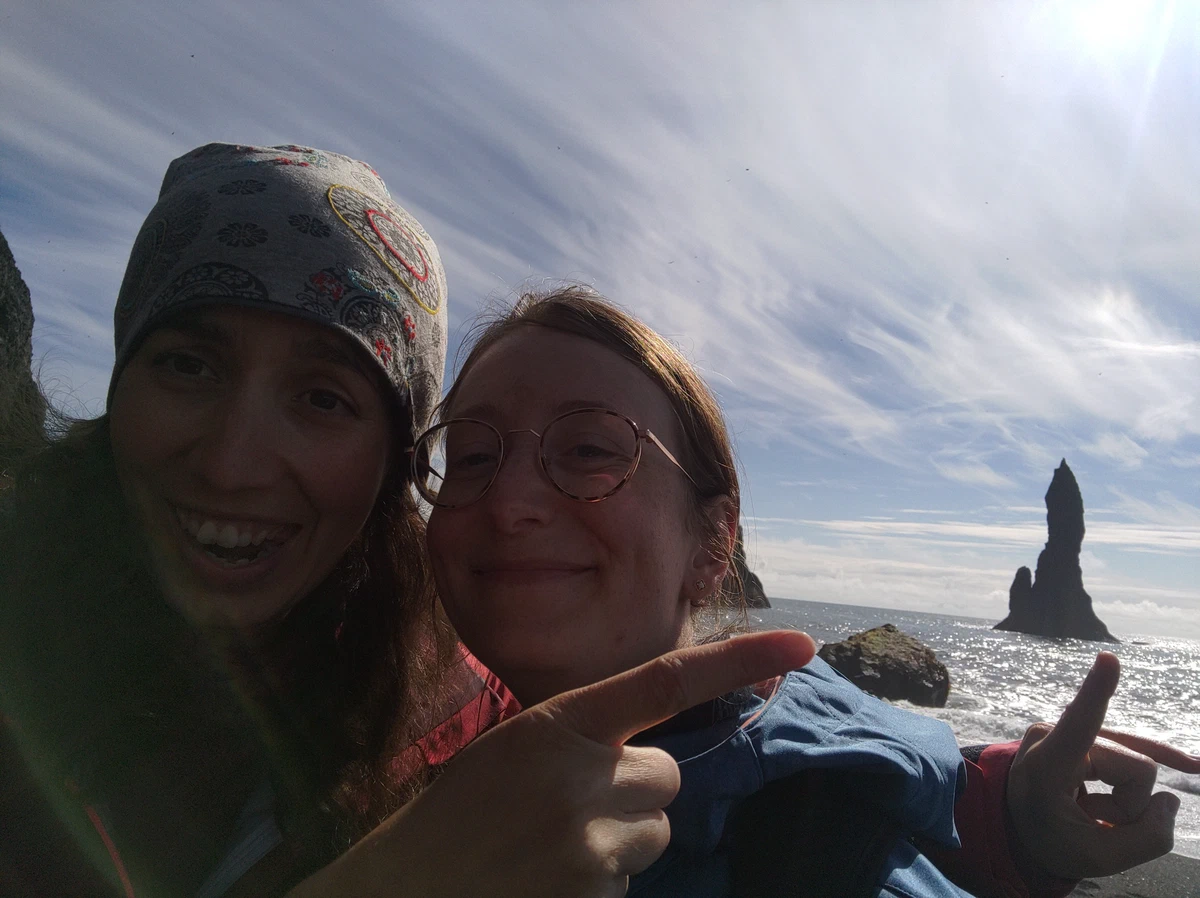 Selfie von zwei lachenden Frauen, die auf die Felsnadel im Meer zeigen