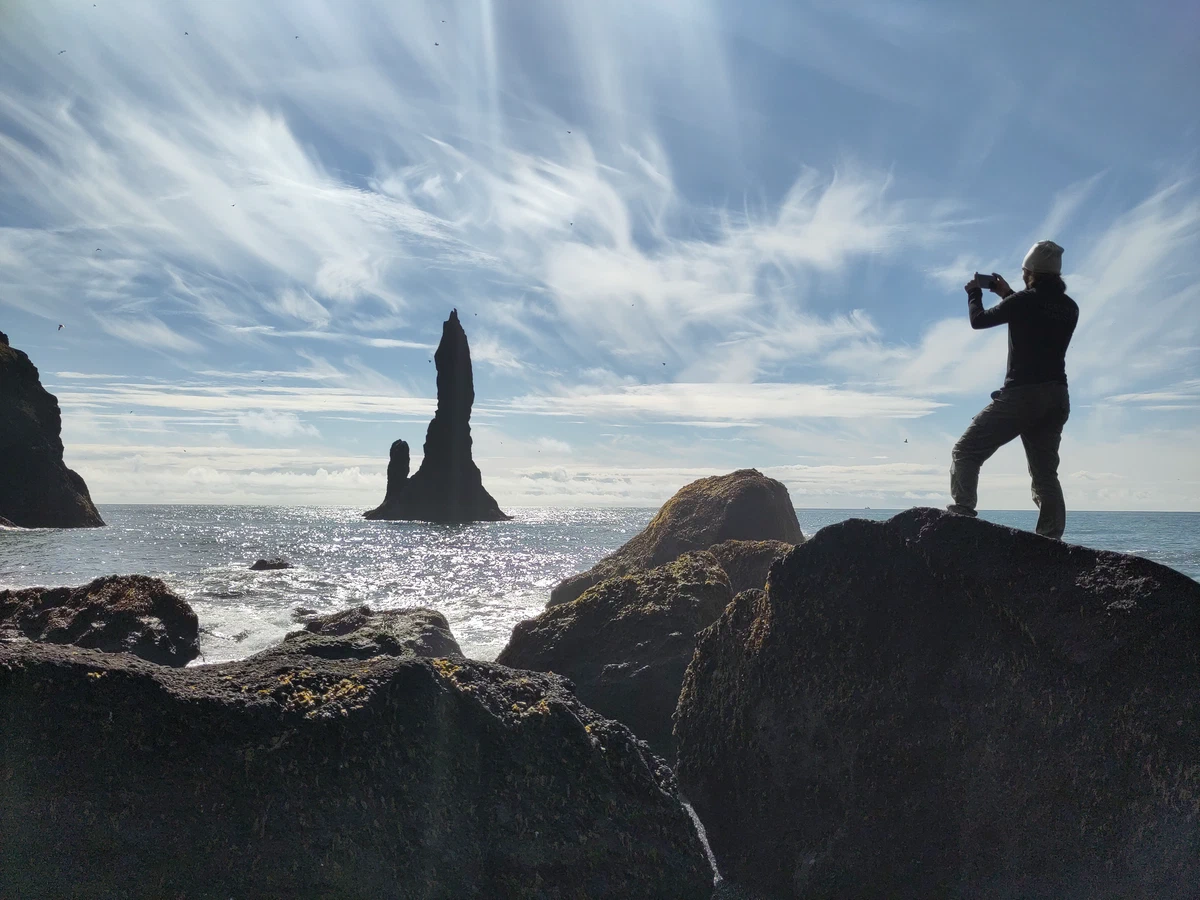 Silhouette einer Person, die auf einem Felsen stehend die Felsnadel fotografiert