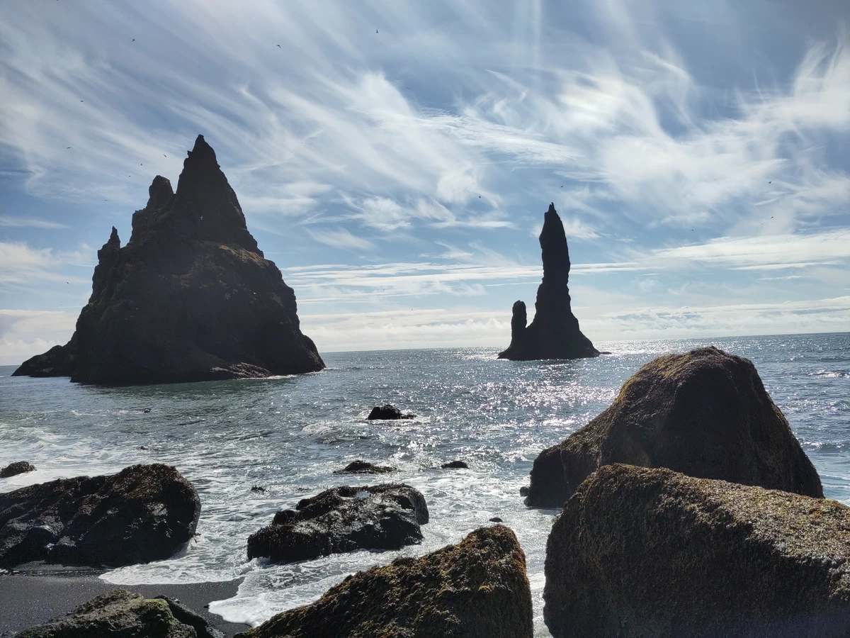 Die Felsnadeln Reynisdrangar ragen hinter rund geschliffenen Felsblöcken aus dem Meer