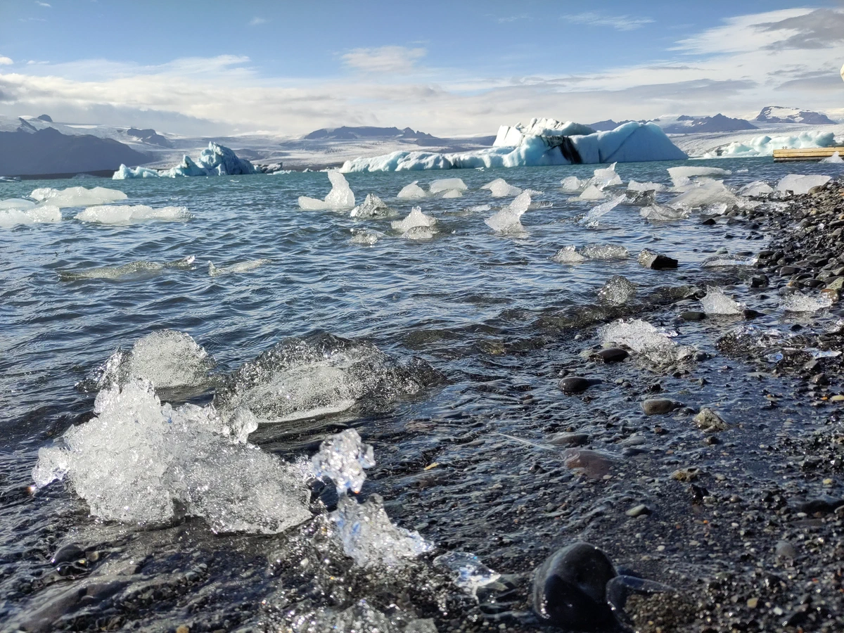 Eisbrocken am Ufer, dahinter größere blaue Eisberge auf dem Wasser