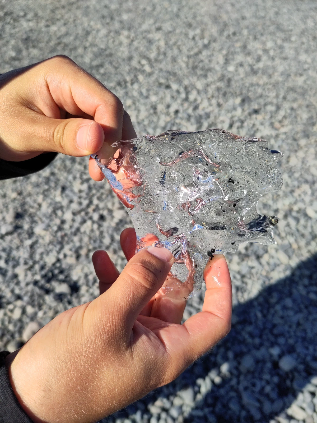 Zwei Hände halten ein glasklares Stück Gletschereis