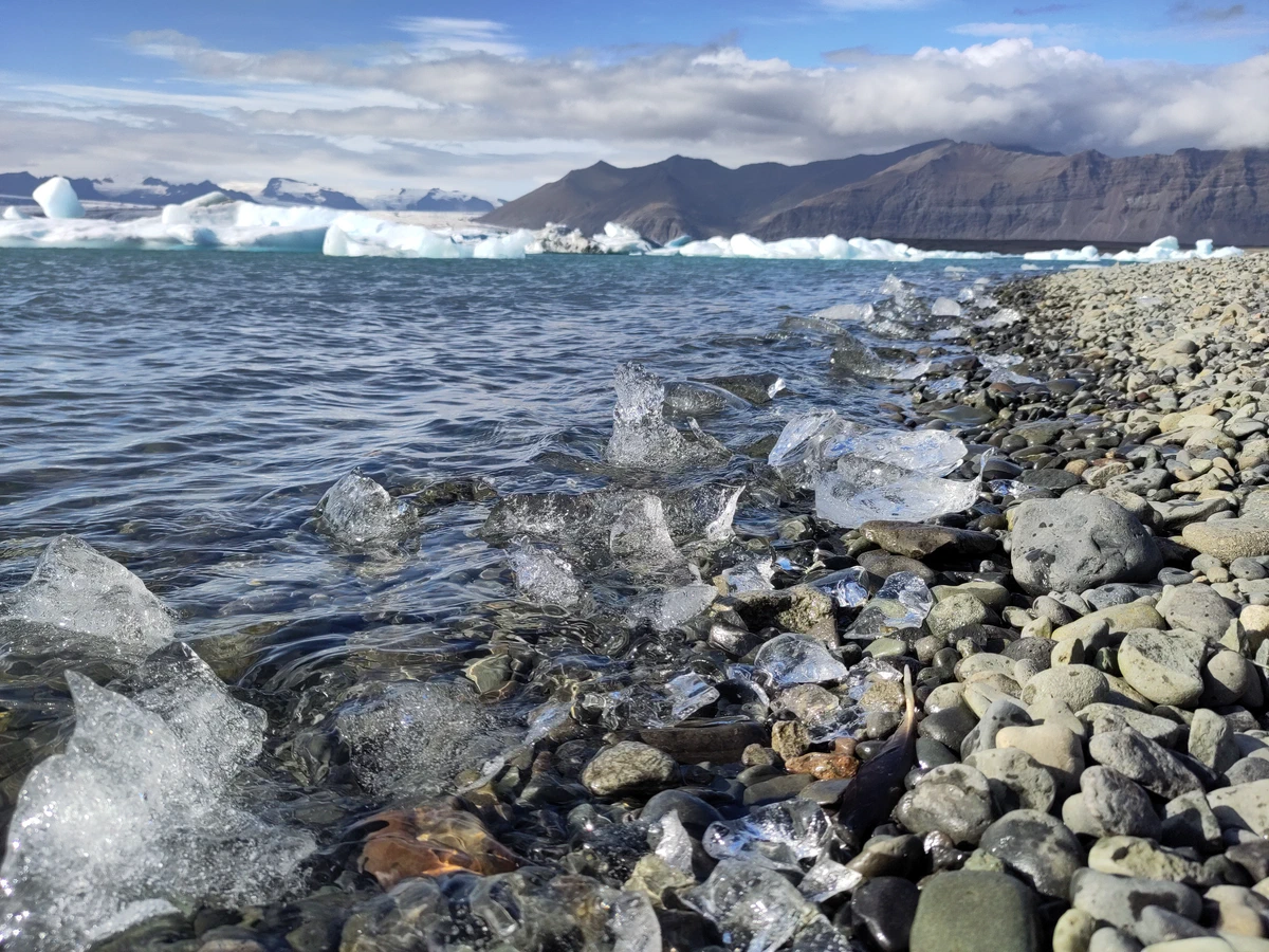 Klare Eisbrocken zwischen runden Kieseln am Wasser