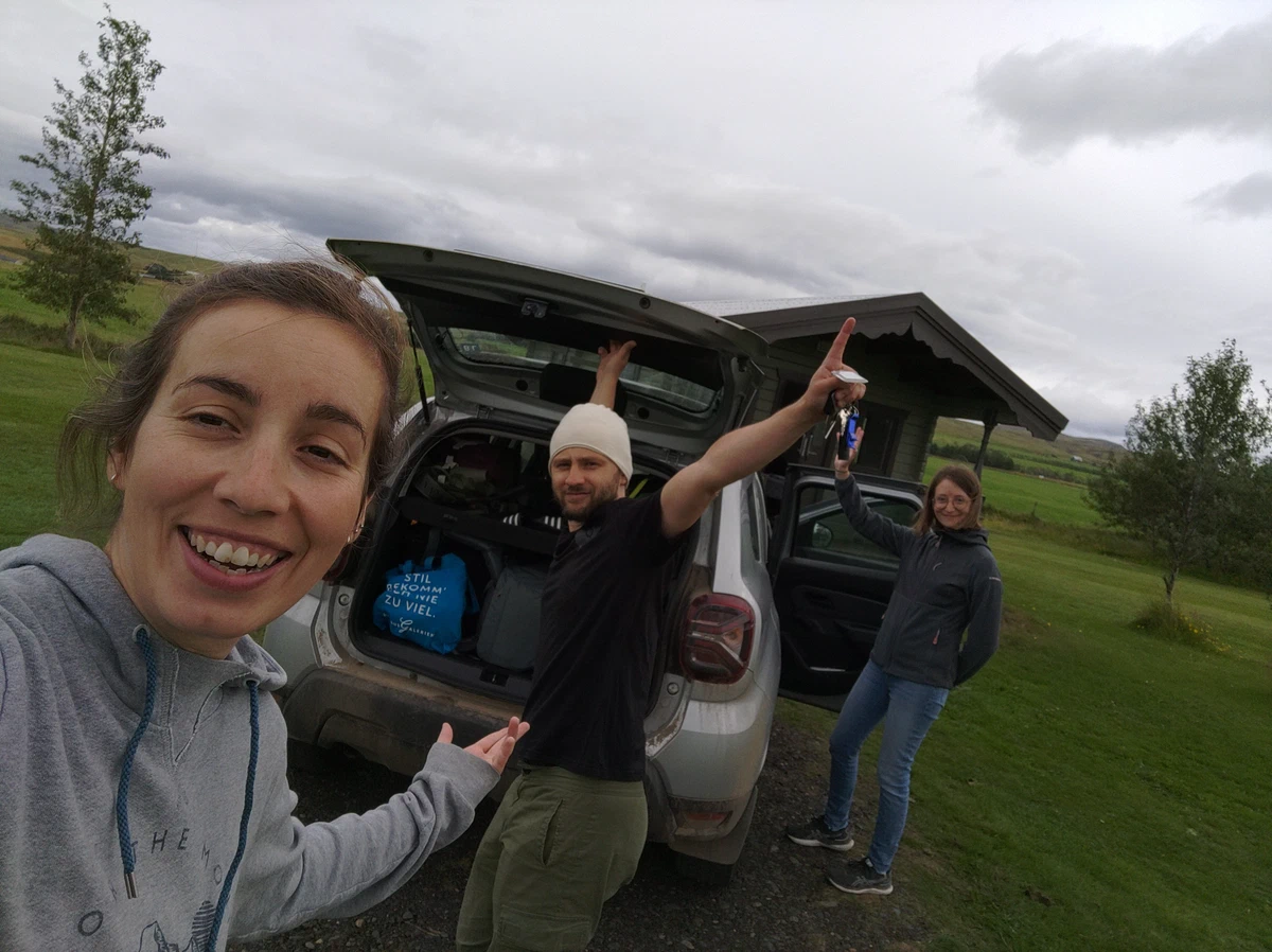Selfie zu dritt am vollgepackten Kofferraum, einer reckt die Arme hoch