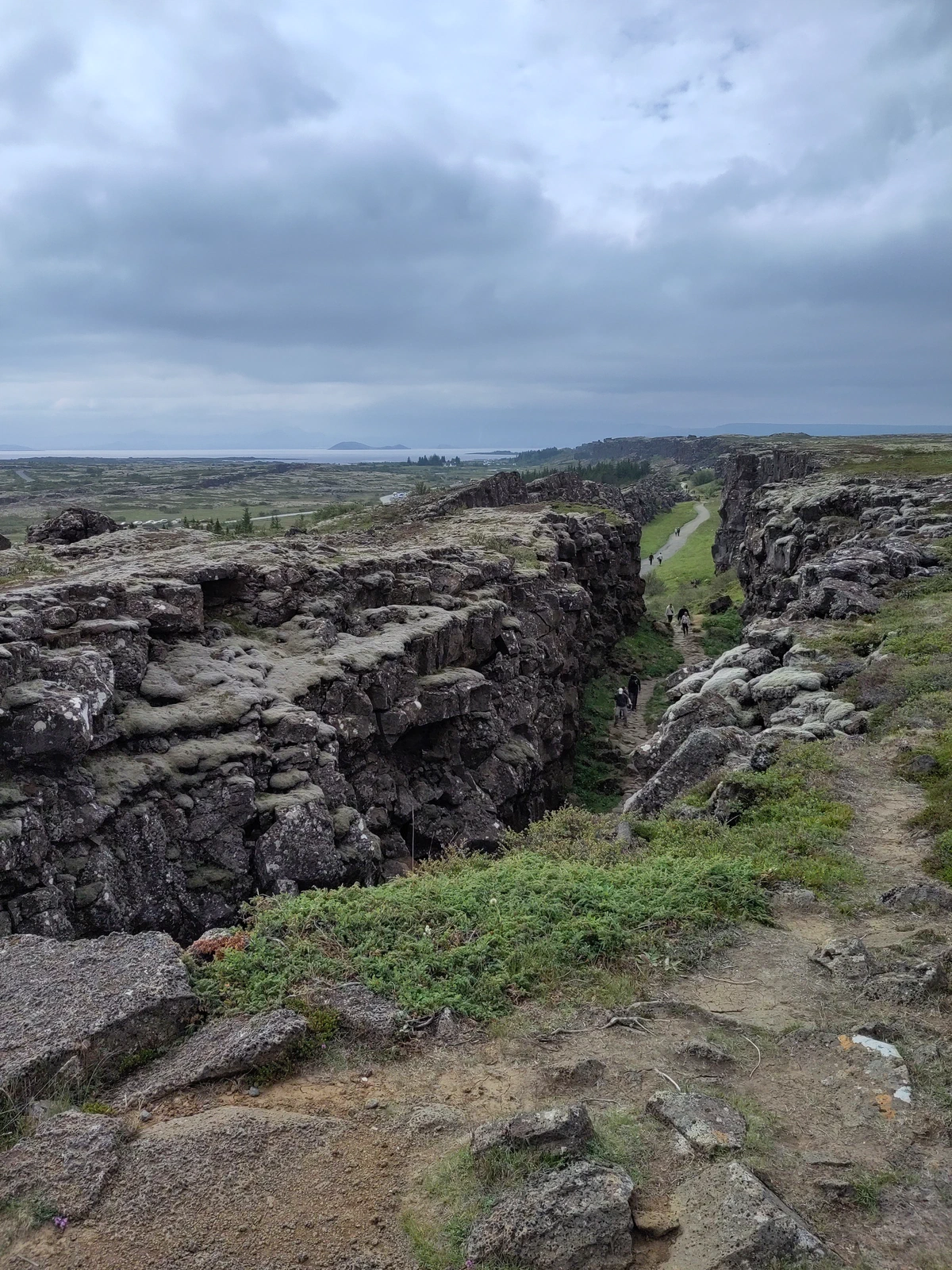 Þingvellir: aufgerissene Erdspalte zwischen dunklen Felswänden, dazwischen Gras