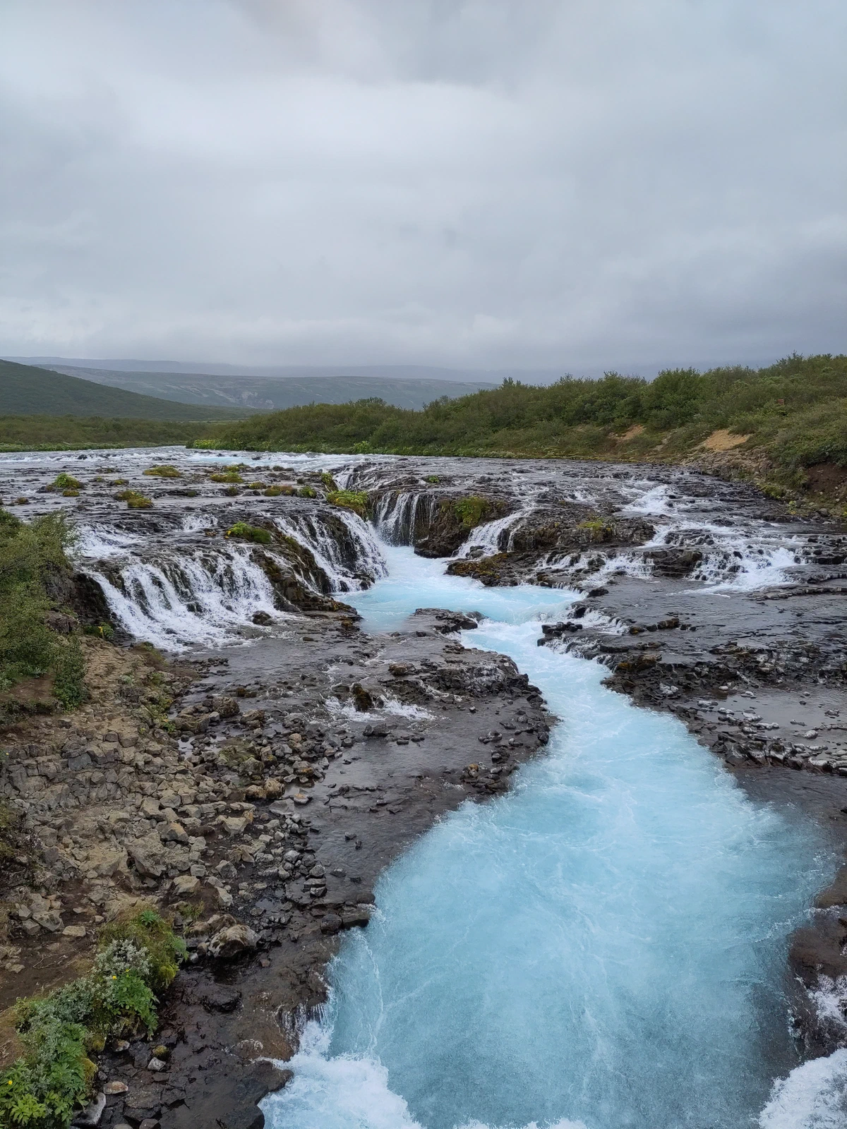 Bruáráfoss: leuchtend türkisblaues Wasser fließt durch eine schmale Rinne zwischen vielen kleinen Kaskaden