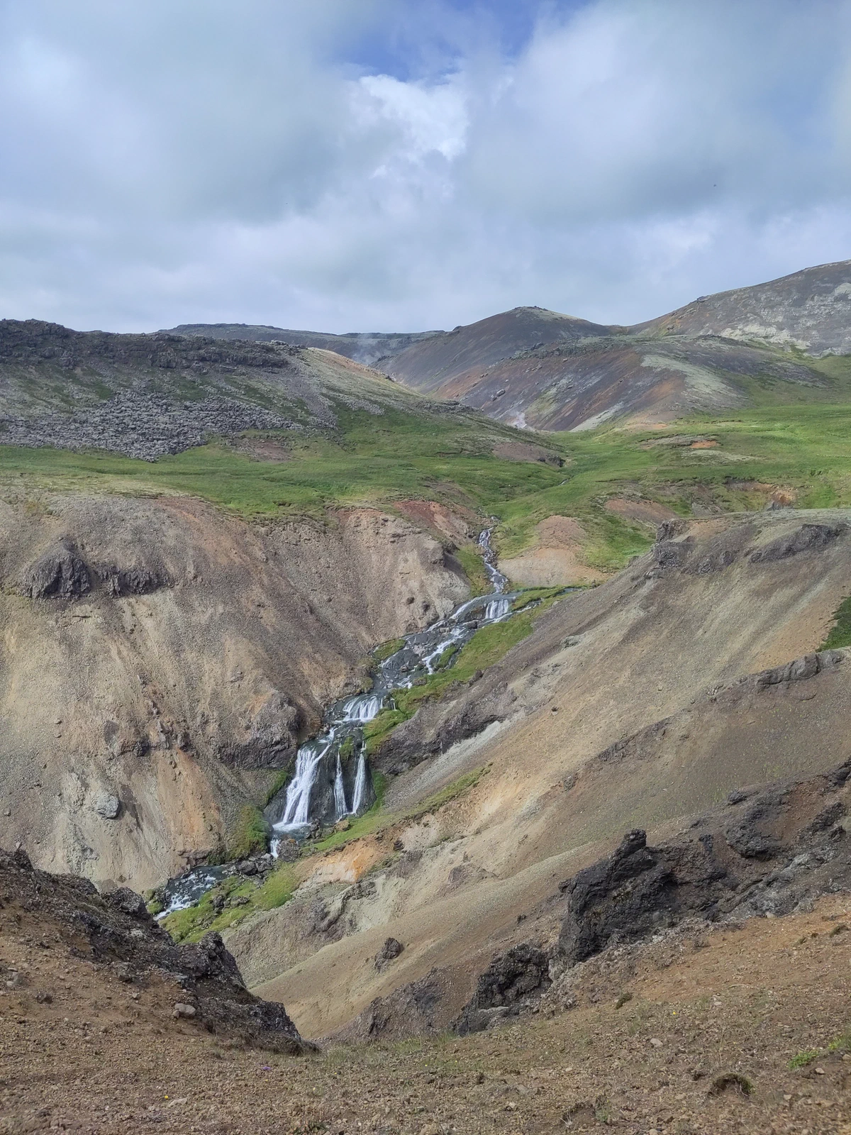 Wasserfall in einer Schlucht zwischen bunten, kahlen Berghängen