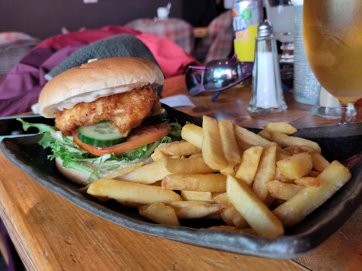 Fischburger mit Pommes auf einem dunklen Teller