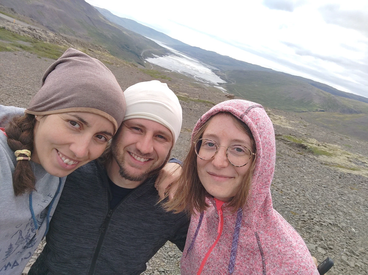 Selfie zu dritt mit Mützen und Kapuze vor einem kargen Berghang
