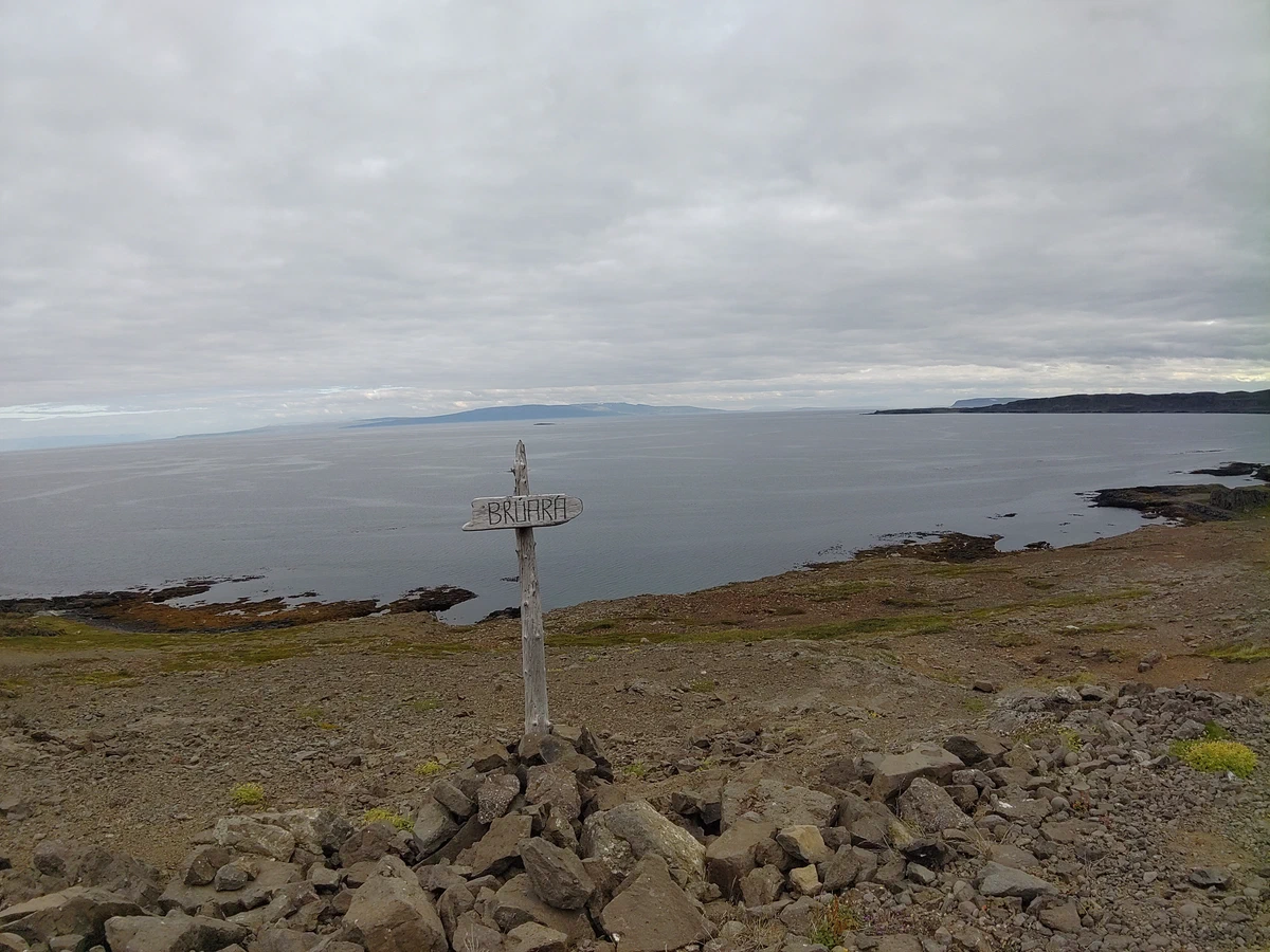 Verwitterter Holzwegweiser auf einem Steinhaufen über einem Fjord