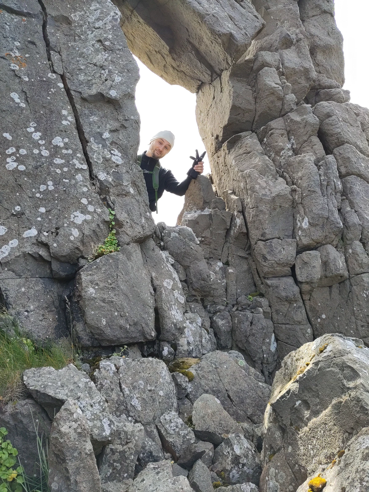 Eine Person schaut winkend durch ein Felsentor aus Basalt