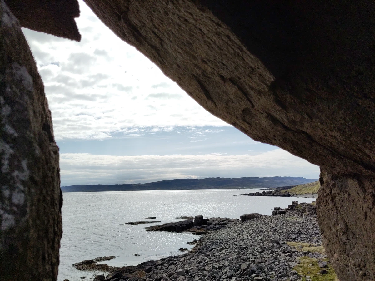 Blick aus einer Felshöhle auf den Fjord und den steinigen Strand