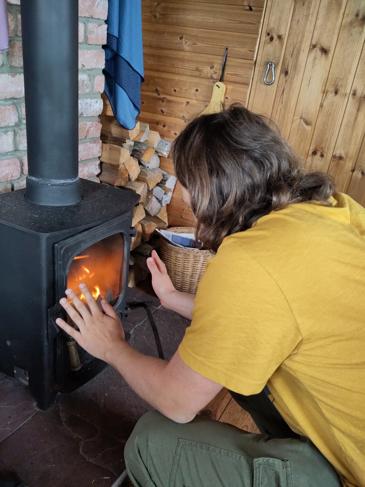 Eine Person kniet vor dem Holzofen und legt Holz nach