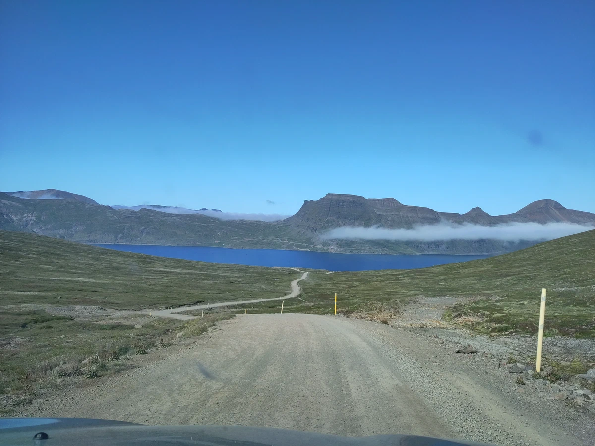 Schotterstraße führt hinunter zu einem tiefblauen Fjord zwischen Tafelbergen