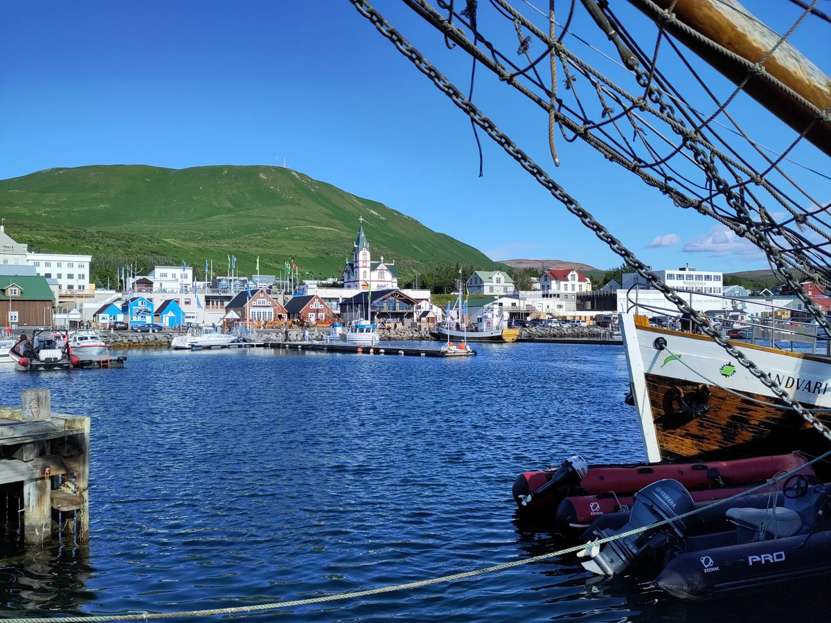 Hafen von Húsavík mit bunten Häusern und der Kirche, rechts die Takelage eines Segelschiffs