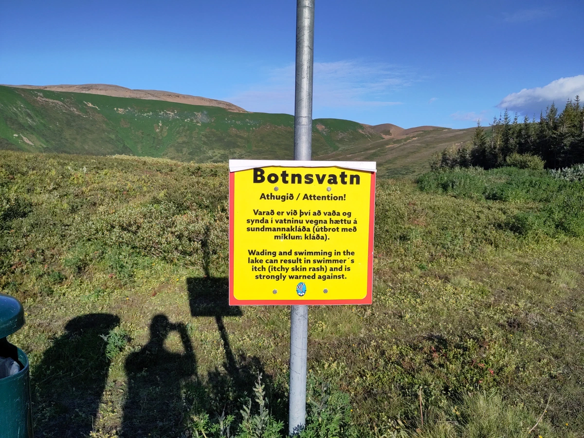 Gelbes Warnschild am Botnsvatn: Baden kann juckenden Hautausschlag verursachen