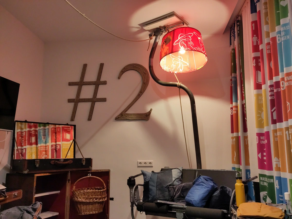 Hotelzimmer mit großer Zimmernummer an der Wand, roter Stehlampe und bunten Vorhängen