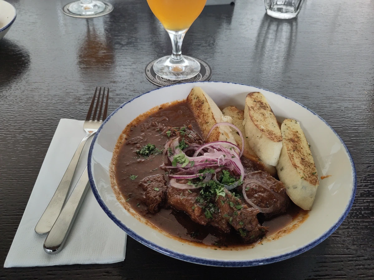 Gulasch mit Knödelscheiben und roten Zwiebeln, dazu ein Bier