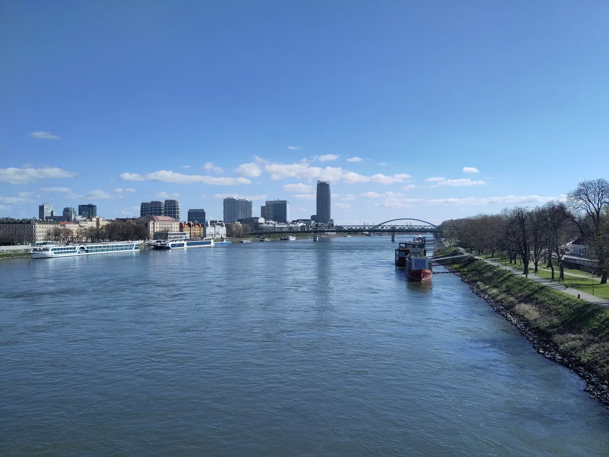 Die breite Donau mit Hochhäusern am Ufer unter blauem Himmel