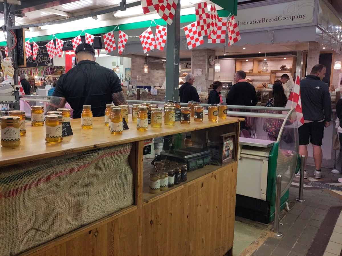 Marktstand mit einer Reihe von Honiggläsern, darüber rot-weiße Wimpel