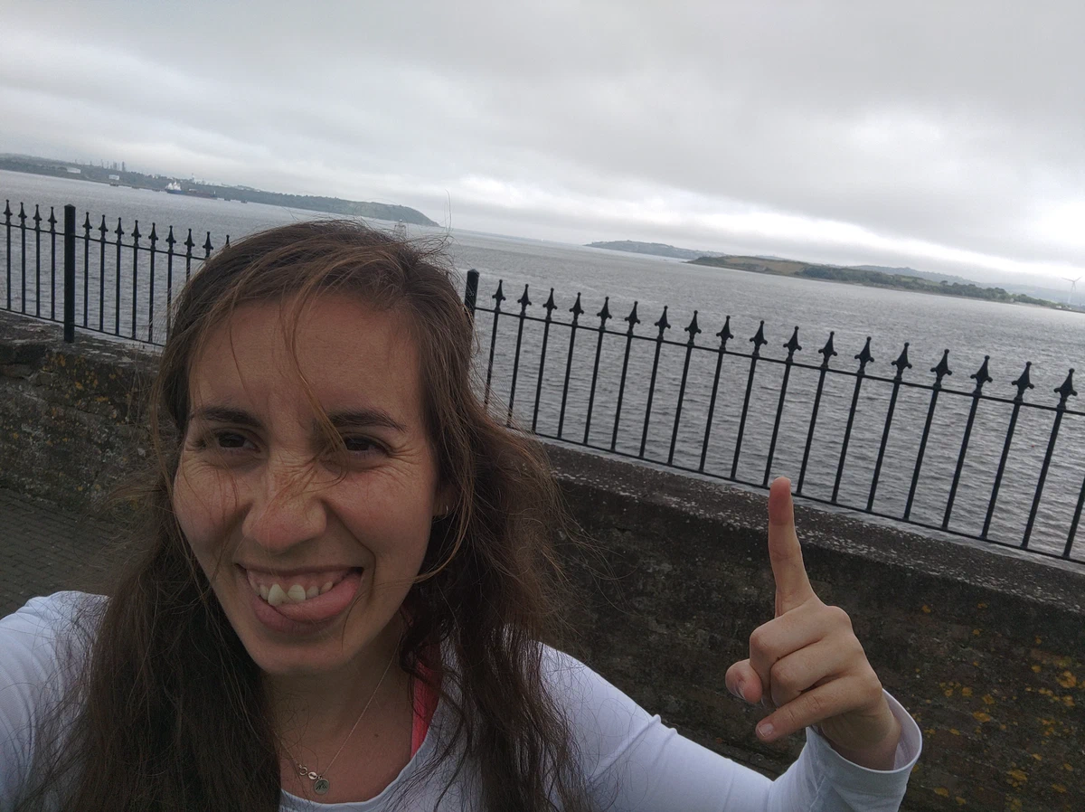 Selfie mit Grimasse und erhobenem Zeigefinger am Geländer über der Bucht