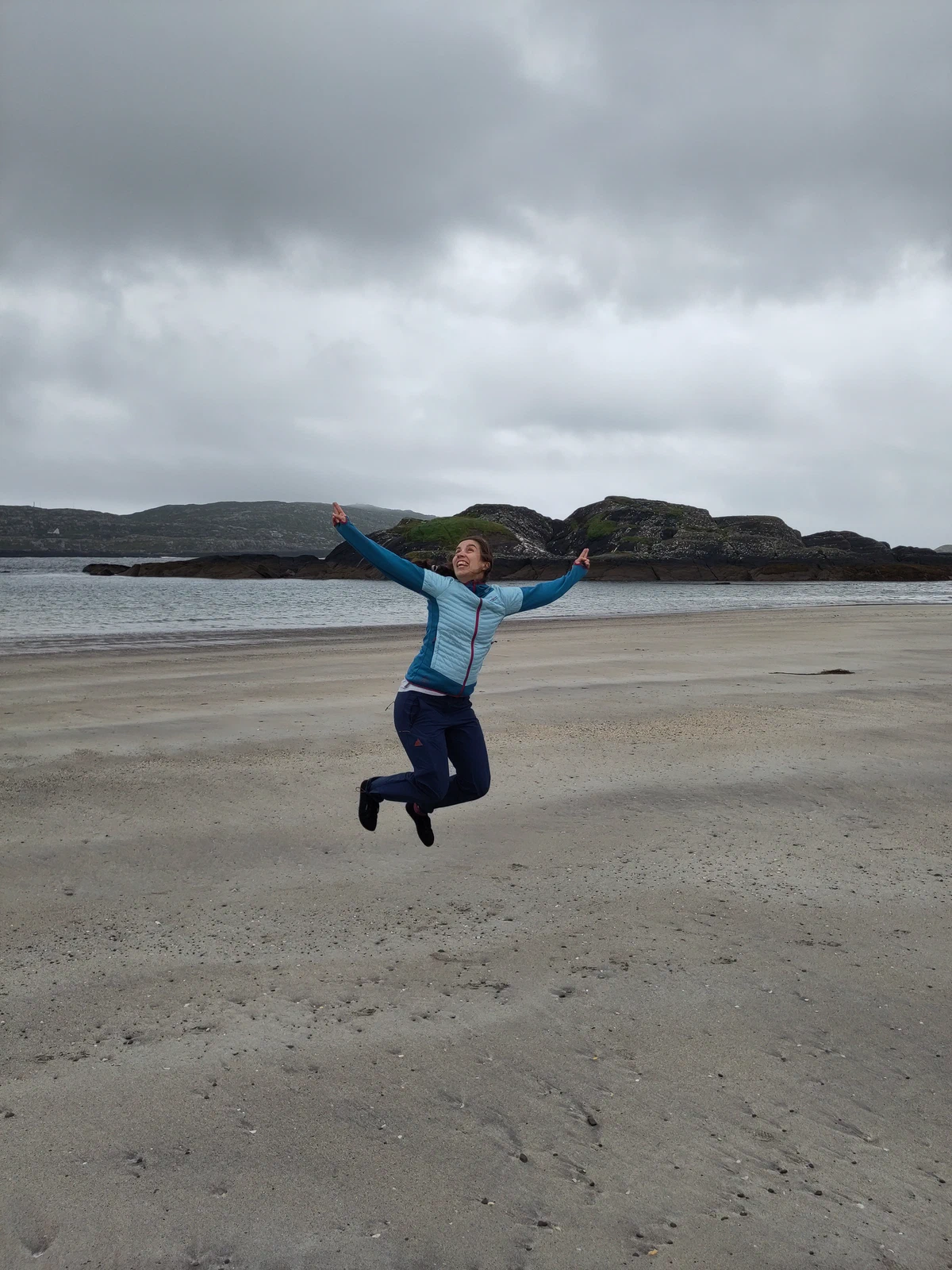 Eine Person springt mit ausgebreiteten Armen am Strand in die Luft