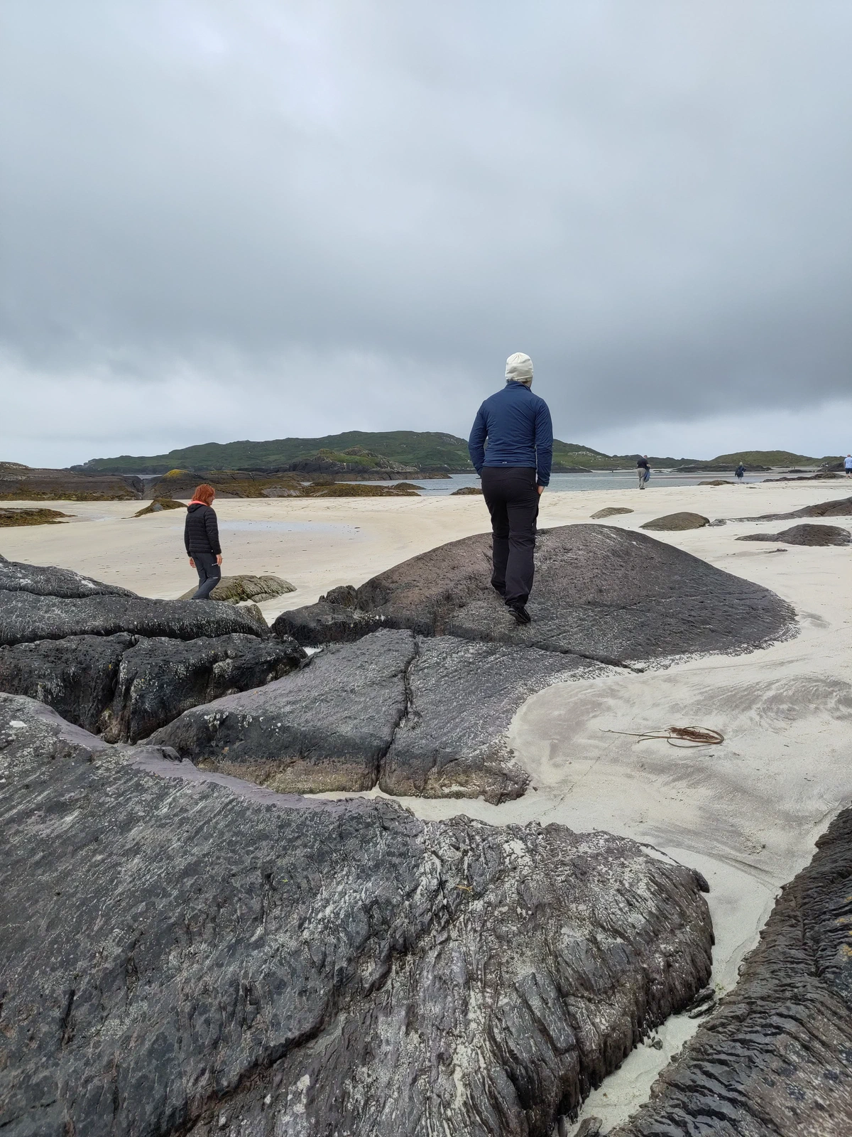 Eine Person steht auf einem runden Felsen am Strand, von hinten gesehen