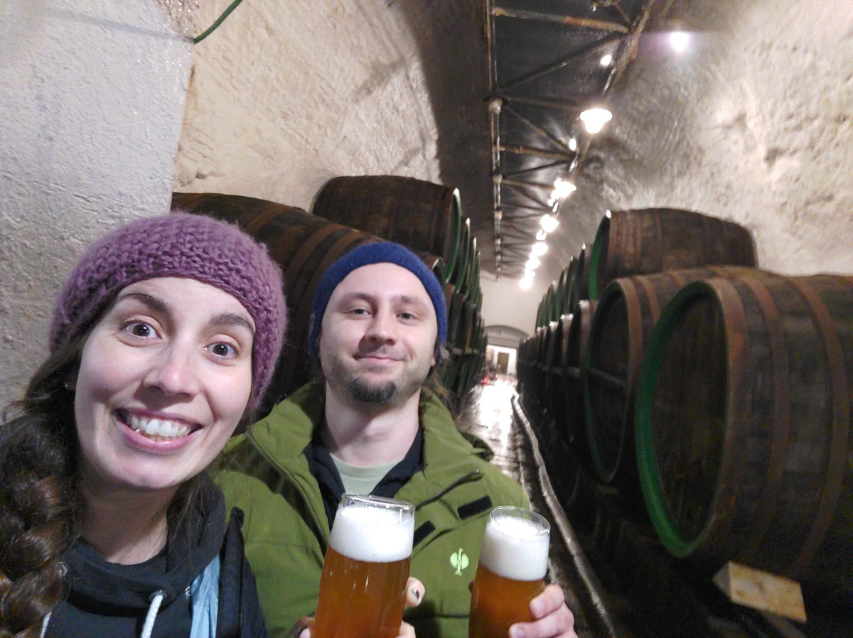 Selfie von uns beiden mit zwei Gläsern Bier vor Holzfässern im Brauereikeller