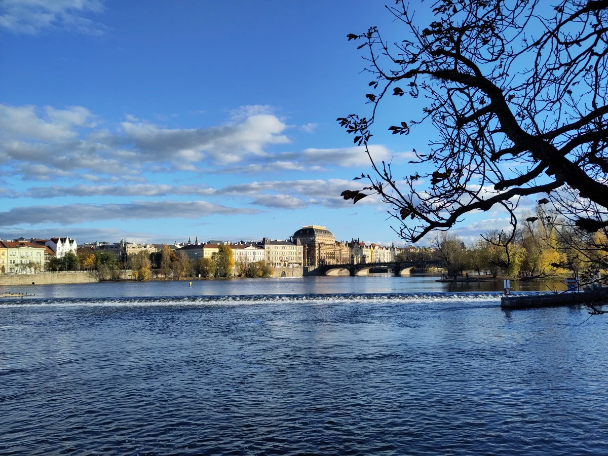 Die Moldau mit einem Wehr, am anderen Ufer das Nationaltheater