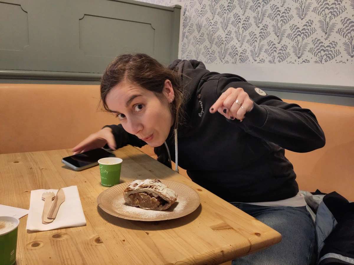Eine Frau beugt sich mit gezückter Faust über ein Stück Strudel am Kaffeehaustisch